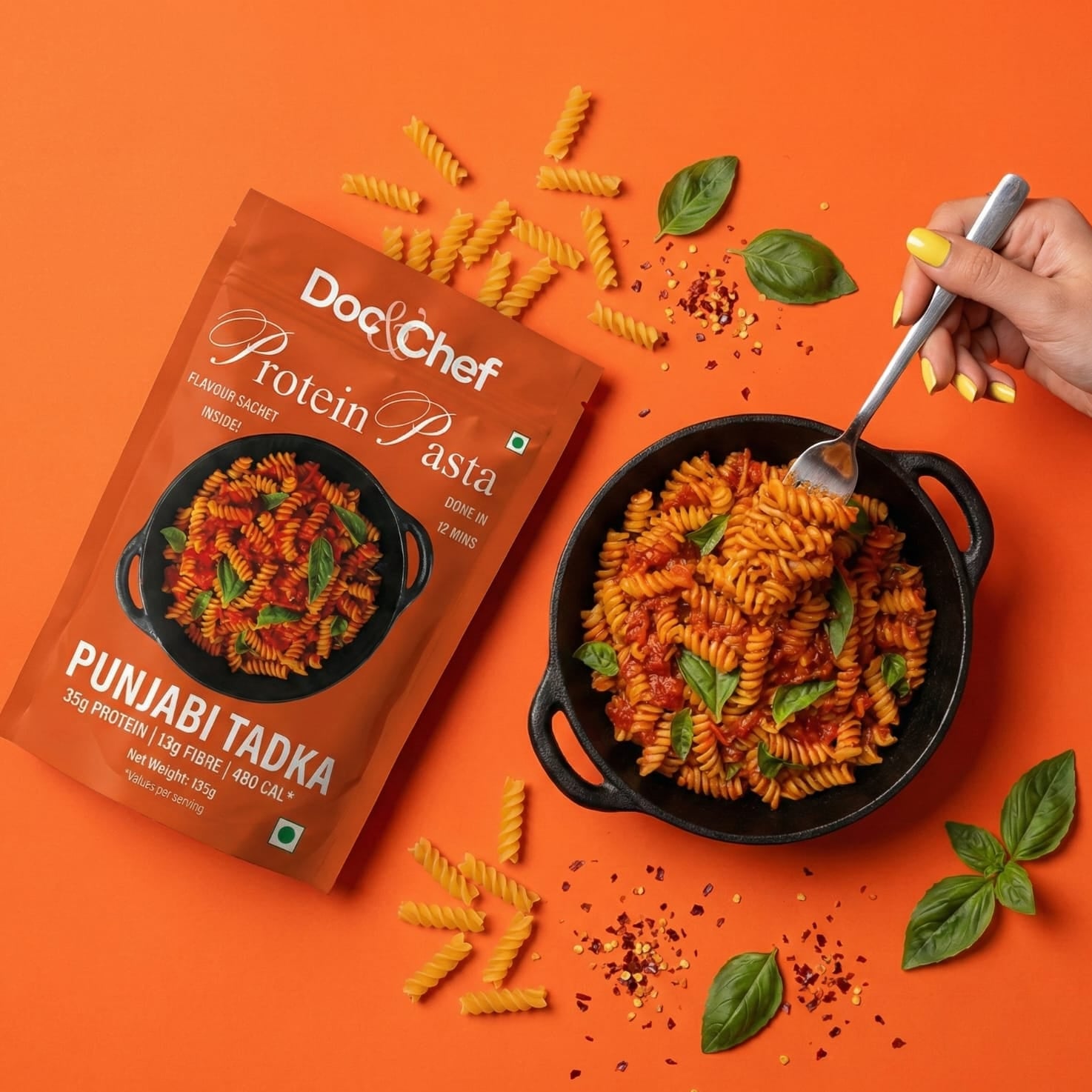 Dodo Chef Protein Pasta Punjabi Tadka with pasta, basil leaves, and a fork on an orange background